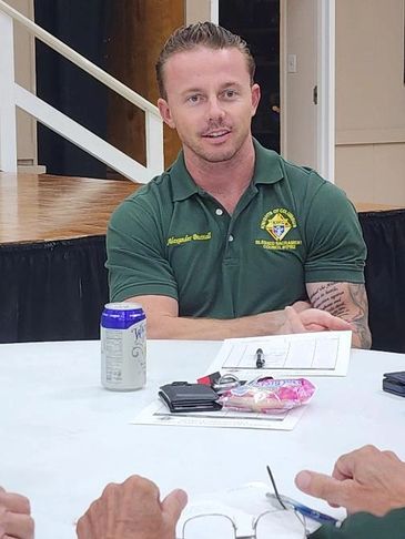 Man in green uniform sitting at a table with documents and a drink.