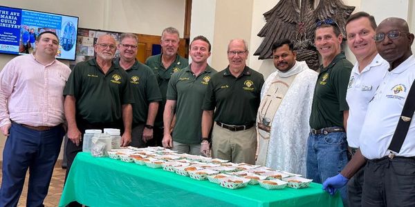 Group of men standing behind a table with prepared food trays in a community setting.
