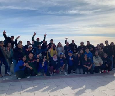 A large group of people posing happily outdoors under a cloudy sky.