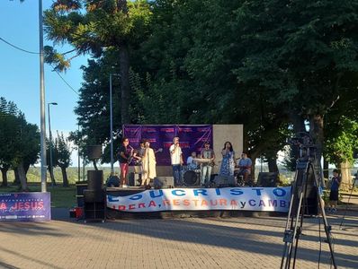 Outdoor musical performance with a group on stage and camera setup.
