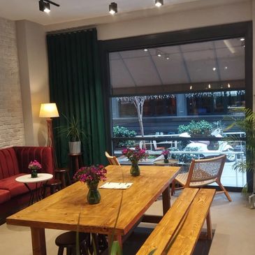 Cozy dining area with wooden tables, green curtains, and a large window overlooking an outdoor space.