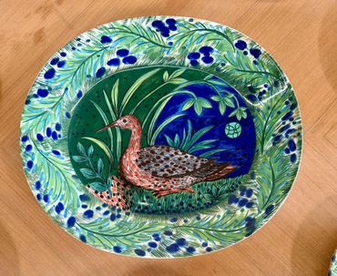 Decorative ceramic plate with a bird and leafy design in green and blue.