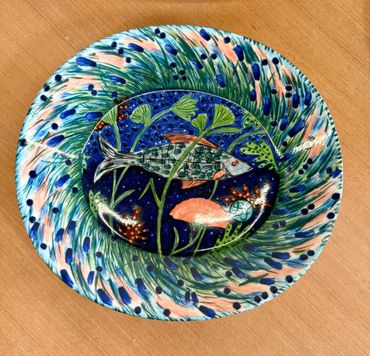 Colorful ceramic plate featuring fish and aquatic plants in a swirling pattern.