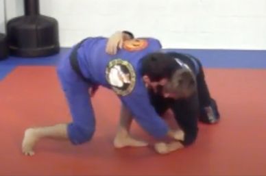 Two martial artists grappling on a mat during training.