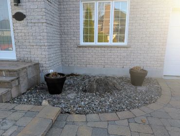 A small garden bed with two flower pots and a tree stump near a house.