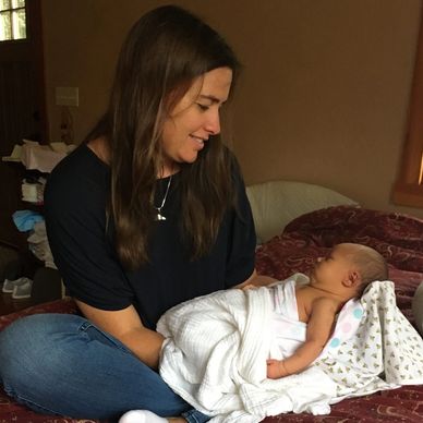 Mujer sonriente sosteniendo a un bebé envuelto en mantas.