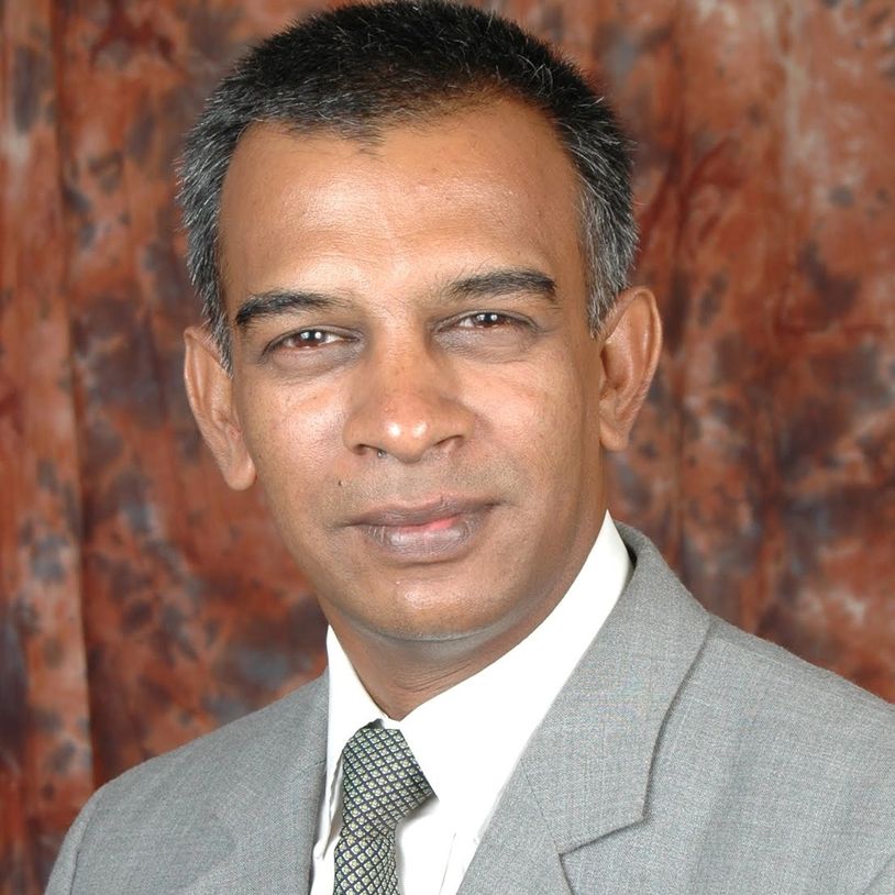Professional man in a gray suit and patterned tie against a brown backdrop.