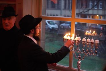 Man lighting a menorah in a dimly lit room.