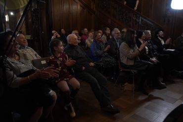 Audience attentively watching an event in a dimly lit room with wooden decor.