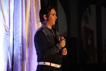 Man holding a microphone, standing by a curtain, smiling.