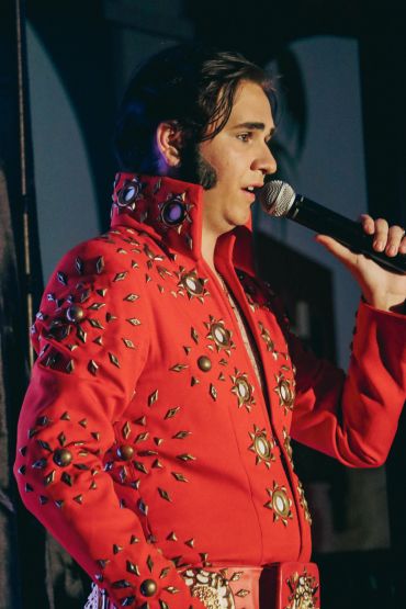 Performer in a studded red jacket singing into a microphone.