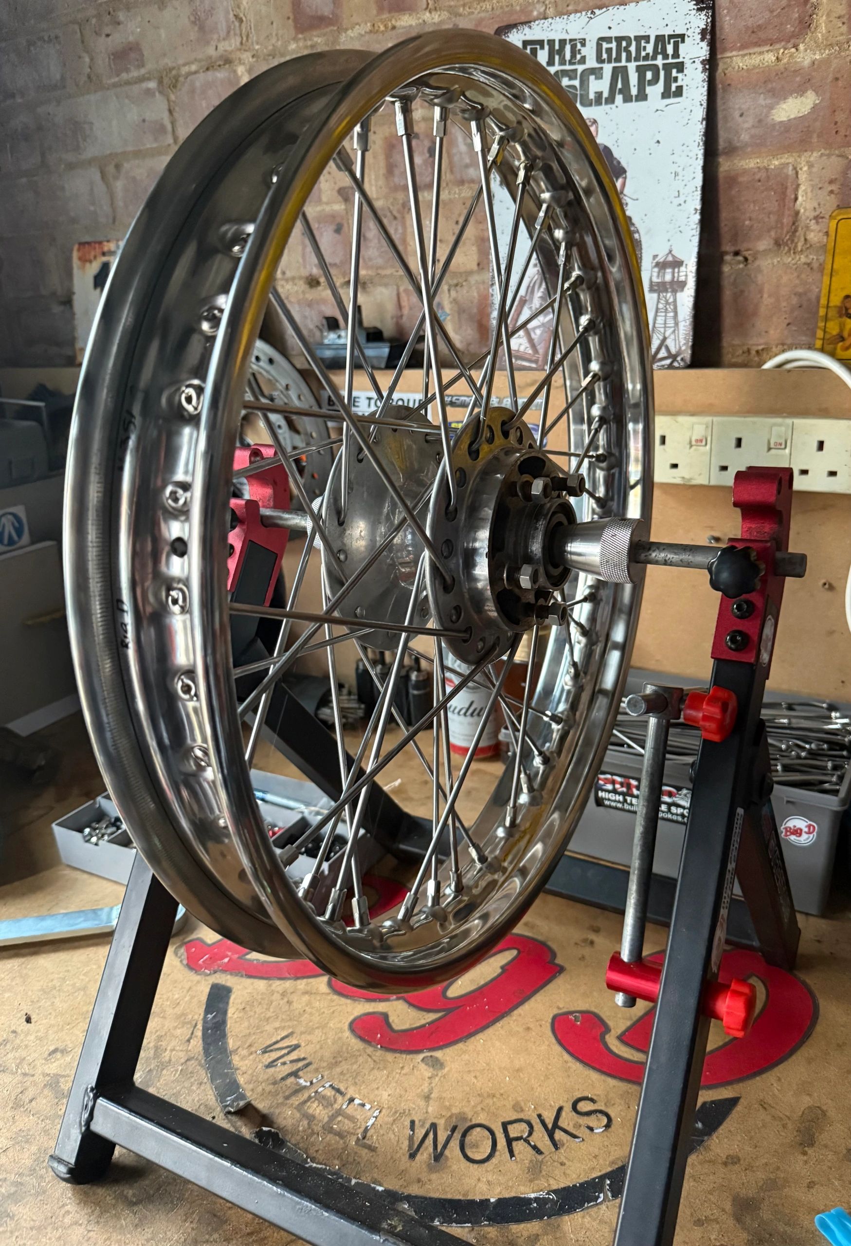 A motorcycle wheel is mounted on a truing stand in a workshop.