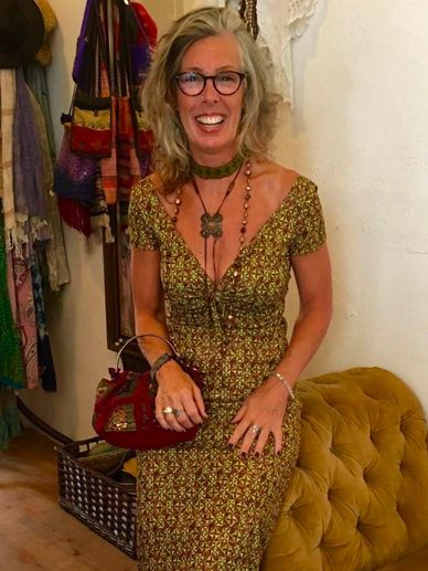 Smiling woman in a patterned dress sitting on a mustard tufted chair.