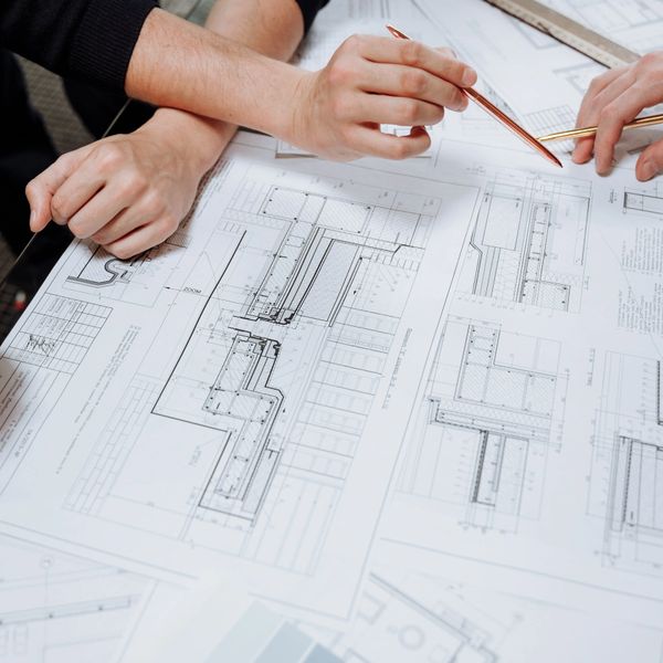 Two people discussing architectural blueprints with pencils.