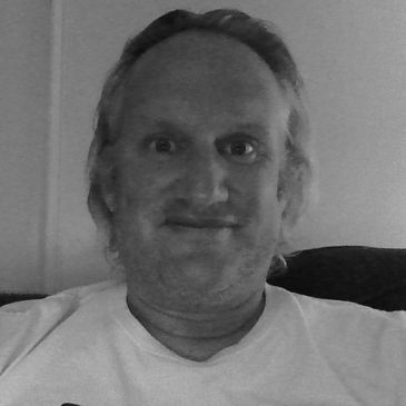 Man with light hair smiling at camera indoors.