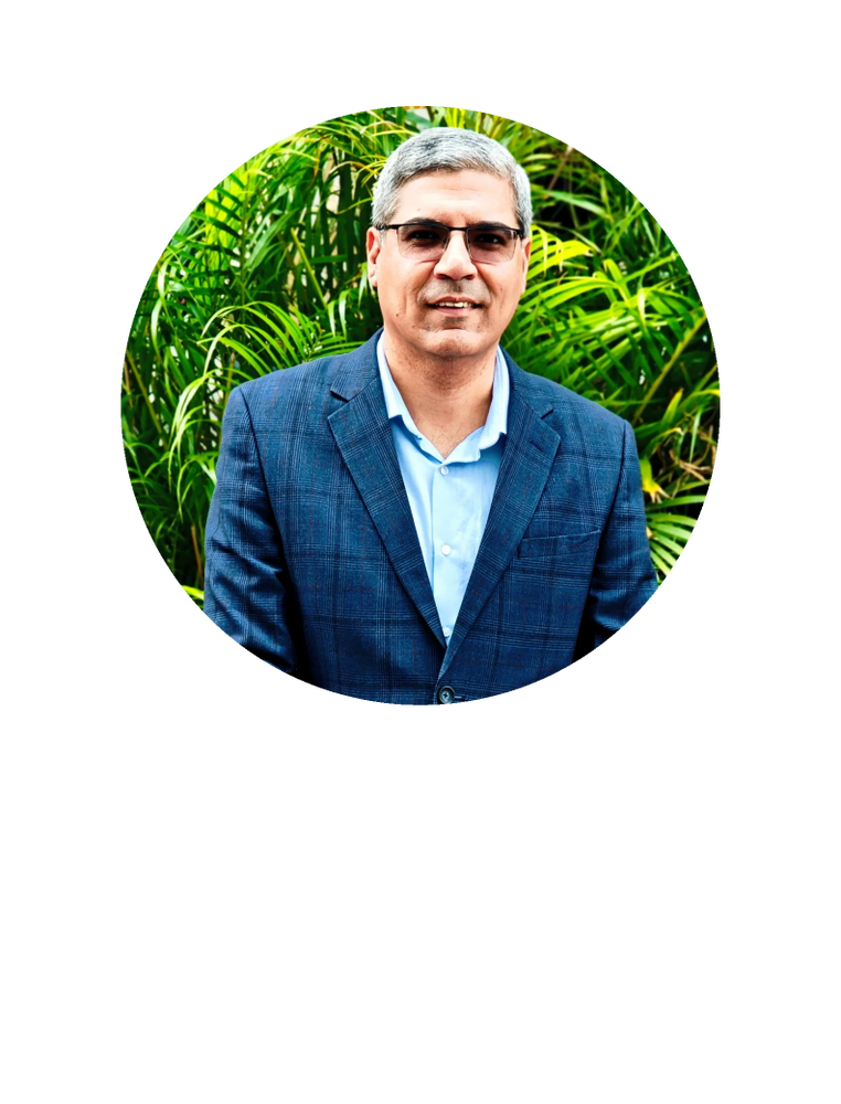 Man in a blue checkered suit stands before green plants.