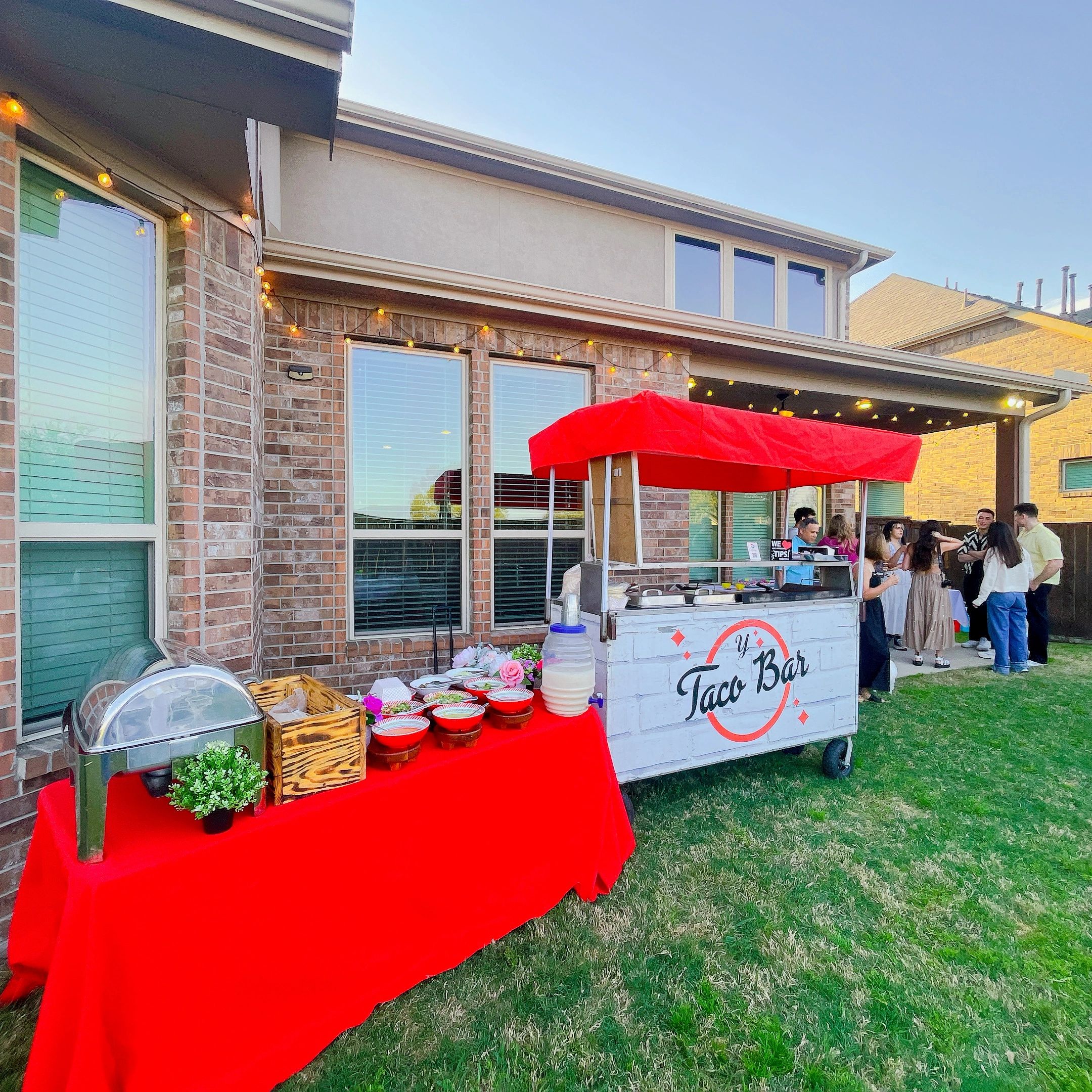 Outdoor/Indoor taco bar setup with people socializing nearby in a backyard.