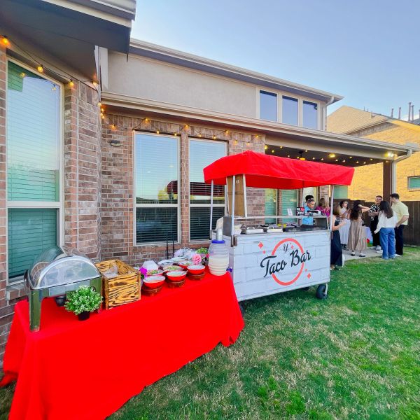 Outdoor taco bar setup with red canopy and buffet table at a backyard party.
