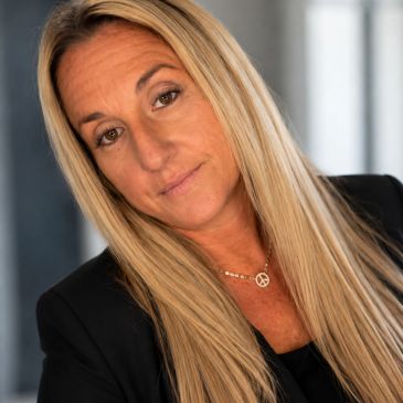 Woman with long blonde hair and a peace necklace.