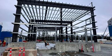 Steel framework construction at an industrial site under cloudy skies.