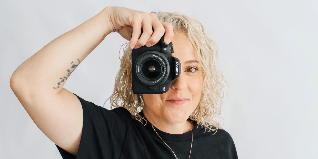 Person with curly blond hair holding a Canon camera.