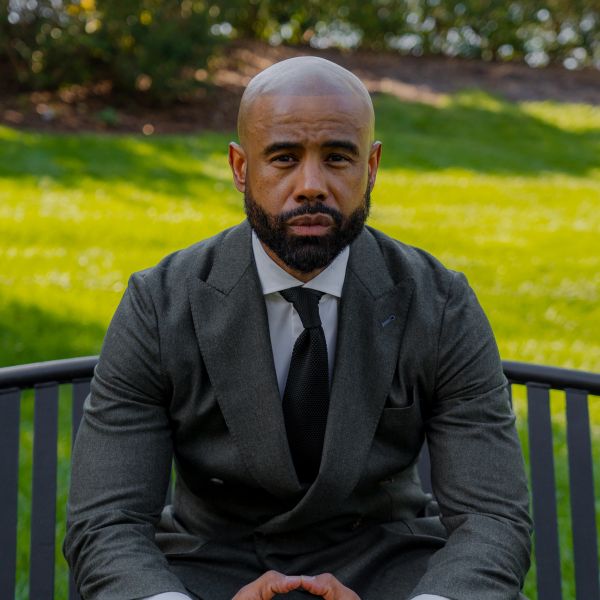 A serious man in a suit sitting outdoors on a bench.