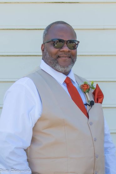 Man in beige vest with red tie and boutonniere.