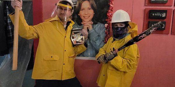 Two people in yellow rain gear, one holding a badge and the other a bat.