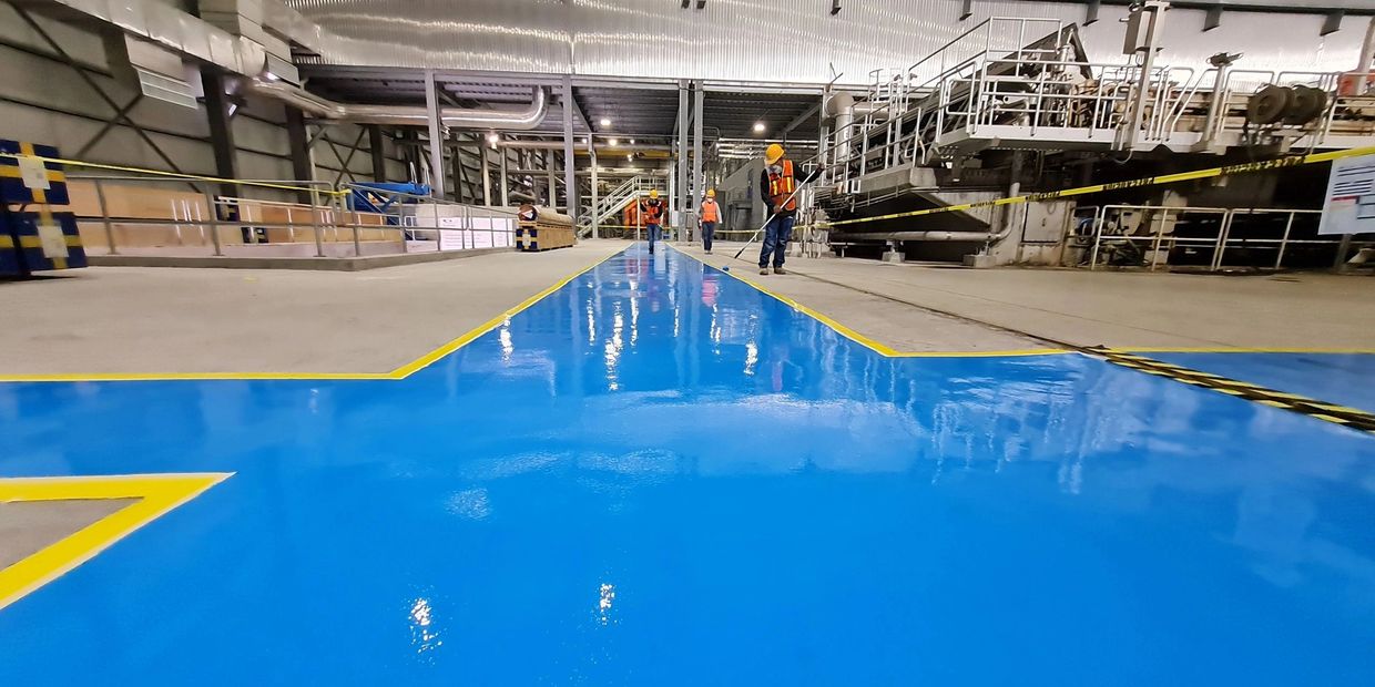 Workers painting a bright blue pathway with yellow borders in an industrial facility.