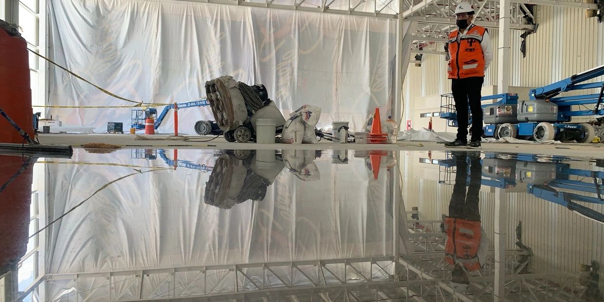 Worker in safety gear stands on polished concrete floor reflecting the surroundings.