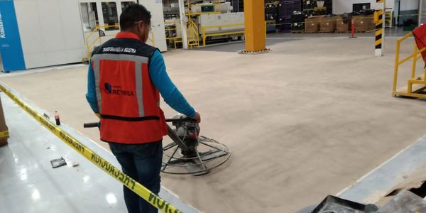 Worker using a power trowel to smooth a concrete floor inside a warehouse.