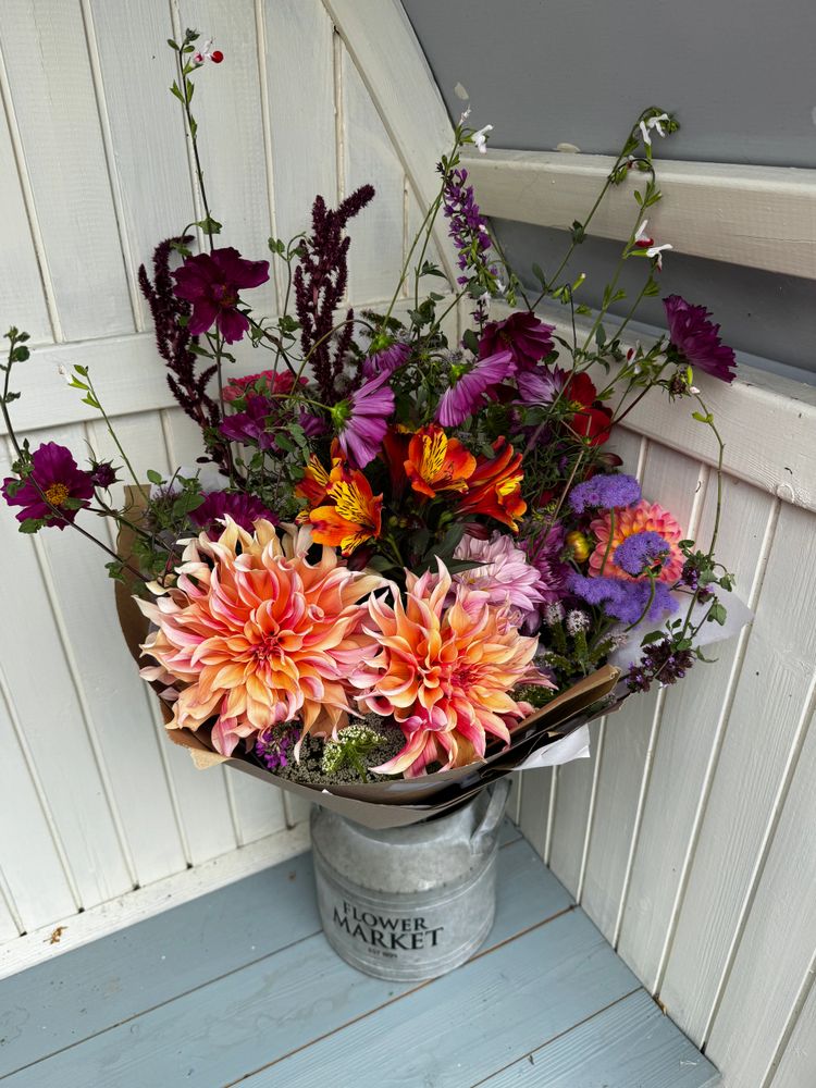 A vibrant mixed flower bouquet in a rustic metal vase labeled 'Flower Market'.