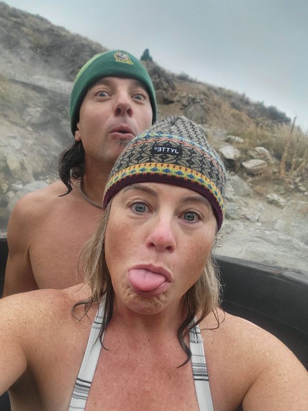 Two people making playful faces outdoors, wearing beanies.
