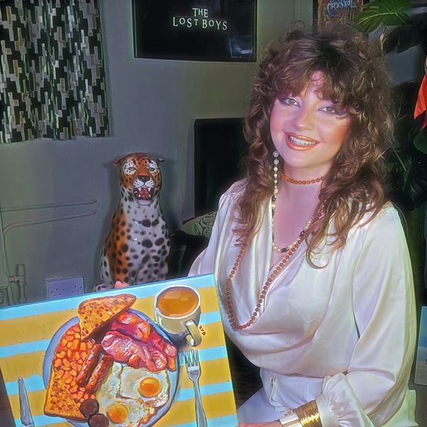Woman with 80s hairstyle smiling next to a painted breakfast plate and a leopard statue.