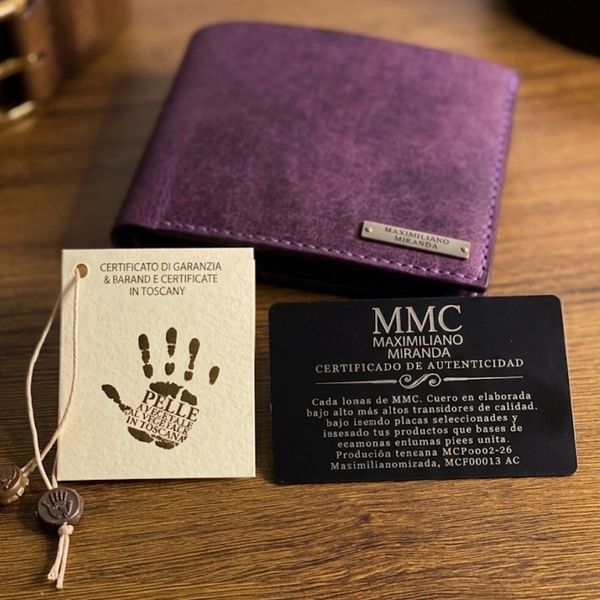 Purple leather wallet with authenticity and guarantee cards on a wooden surface.