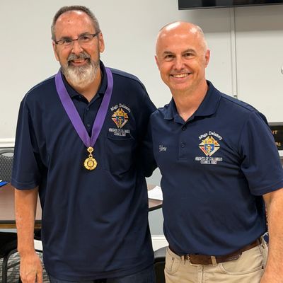 Two men wearing blue shirts with medals and logos, smiling.