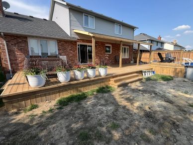 Backyard wooden deck with potted plants and a house in the background.
