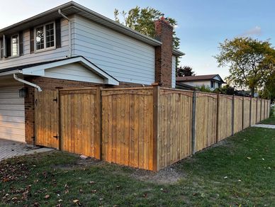 A wooden fence surrounding a house with a garage on a sunny day.