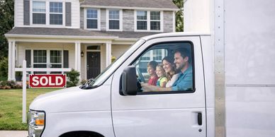 A family in a moving truck in front of their sold house.