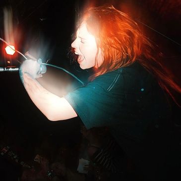 A passionate singer with red hair performs energetically on stage at night.