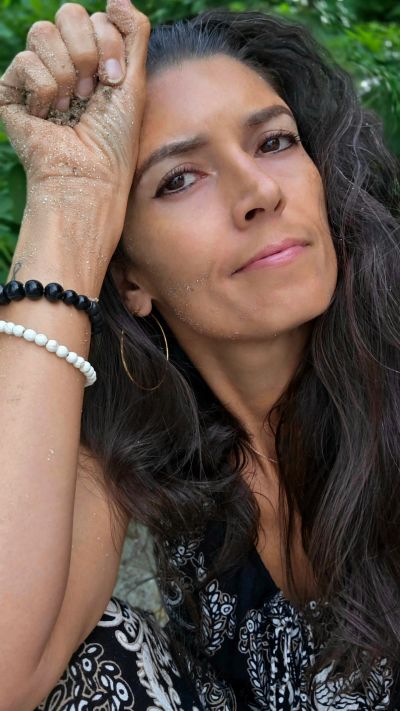 Woman with long hair and sandy hands posing outdoors.