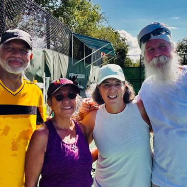 Four adults smiling outdoors beside a tennis court.