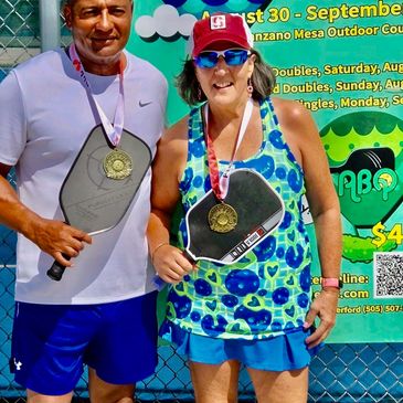 Two people holding pickleball paddles with medals.