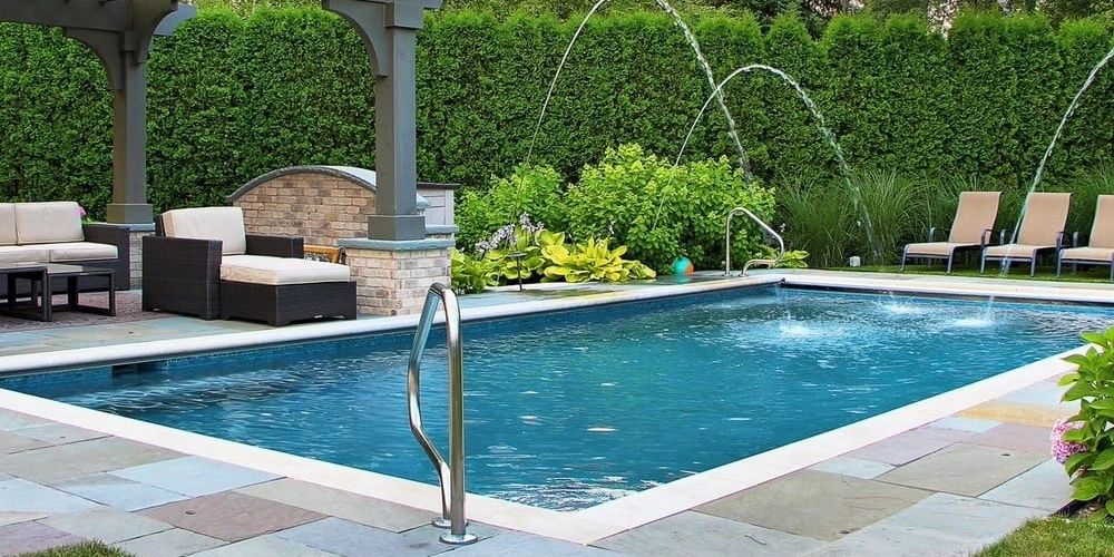 A serene backyard pool with water fountains and comfortable seating under a pergola.
