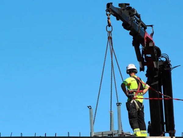 Worker in safety gear overseeing crane lifting.