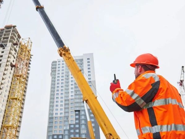 Construction worker with walkie-talkie near cranes and buildings.