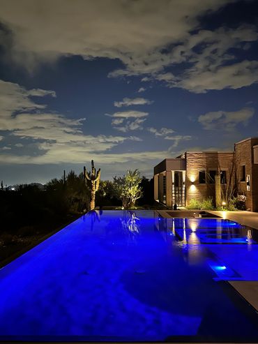 Nighttime pool with blue lights and desert plants.