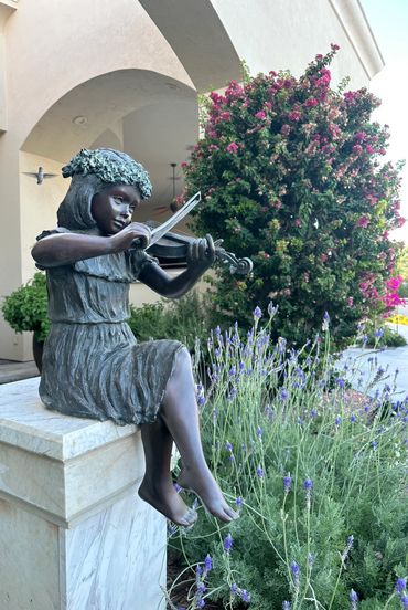 Bronze statue of a girl playing violin outdoors.