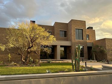 Modern brick house with greenery and cloudy sky.