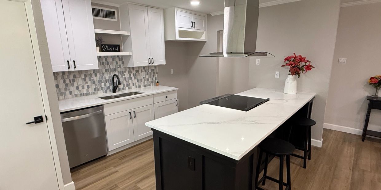 Modern kitchen with white cabinets, a black island, and wooden flooring.